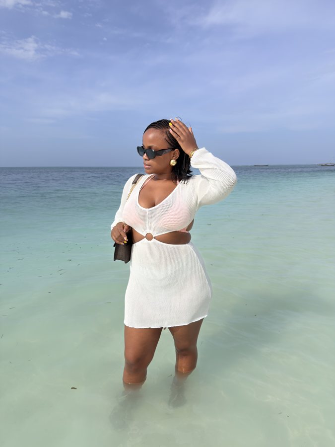 Izuba in sunglasses and a white beach cover-up beside turquoise water